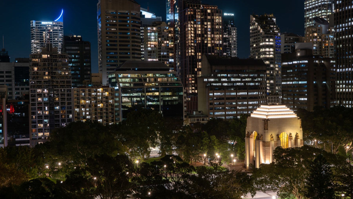 Sydney's illuminated ANZAC War Memorial stands among Hyde Park and the city skyline at night.