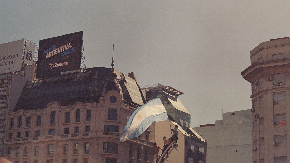 A large Argentine flag waves above football supporters gathered among the historic buildings of Buenos Aires.