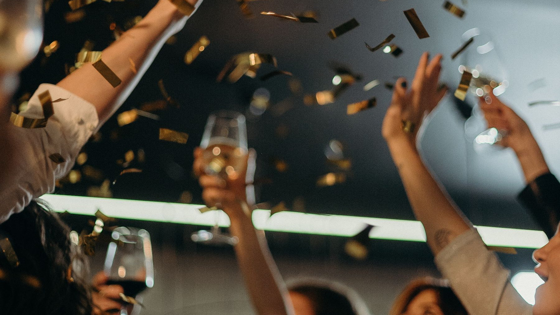 Friends raise sparkling wine beneath falling gold confetti during a New Year's Eve celebration.