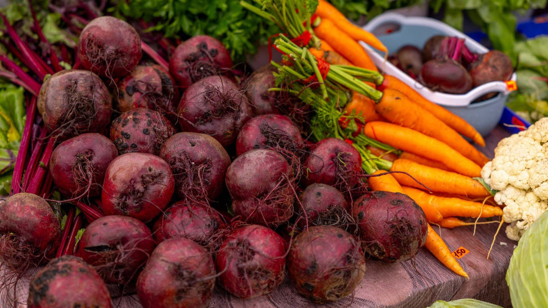 Fresh beets, carrots and cauliflower are displayed together at a produce market.