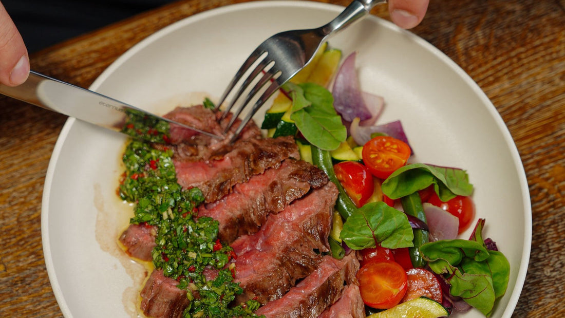 Sliced grilled steak is served with bright green chimichurri and seasonal vegetables.