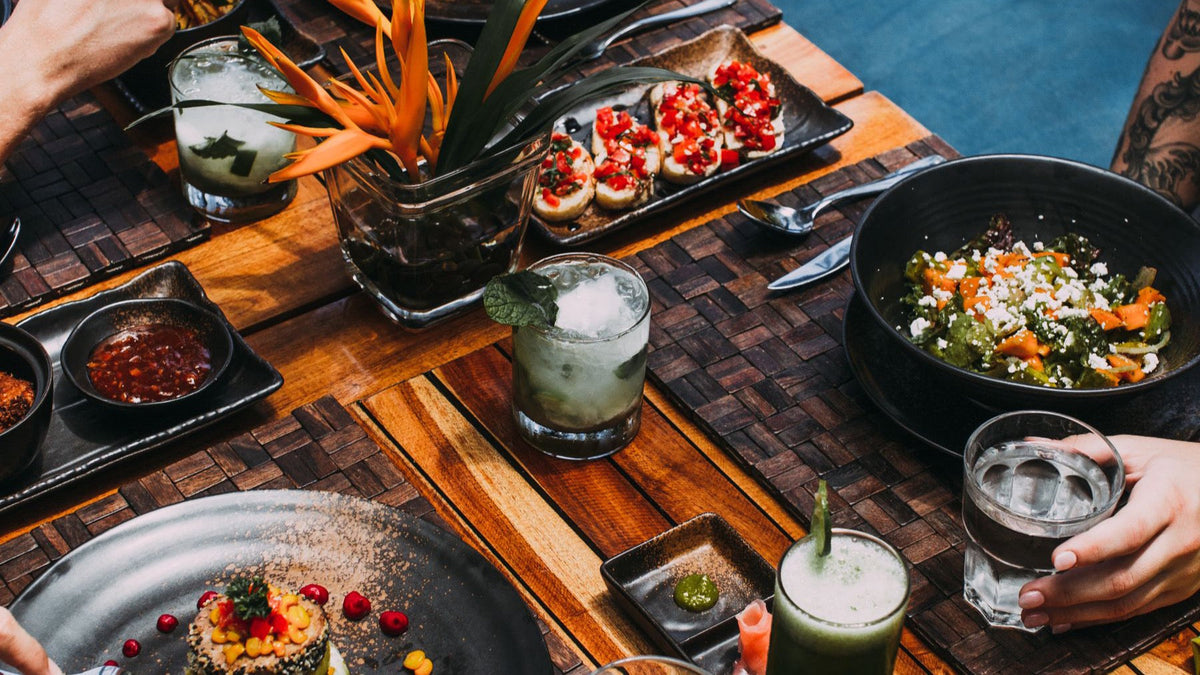 A colourful selection of dishes and drinks is shared around a restaurant table.