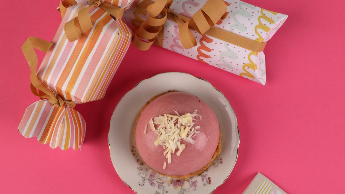 Colourful wrapped gifts and a pink dessert are arranged on a bright celebratory table.