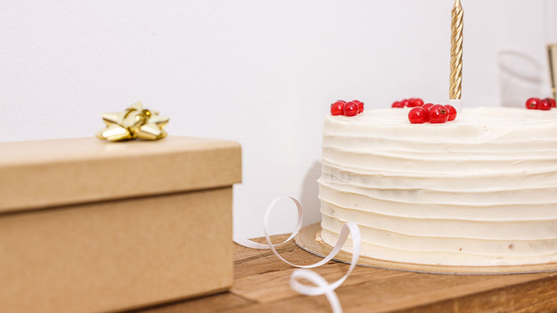 A white celebration cake with red berries sits beside a wrapped birthday gift.