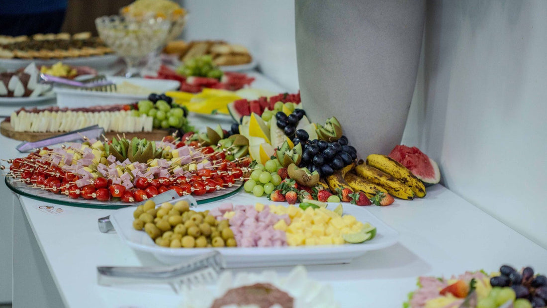 A long buffet presents fruit, cheese, vegetables and appetisers for a large catered gathering.