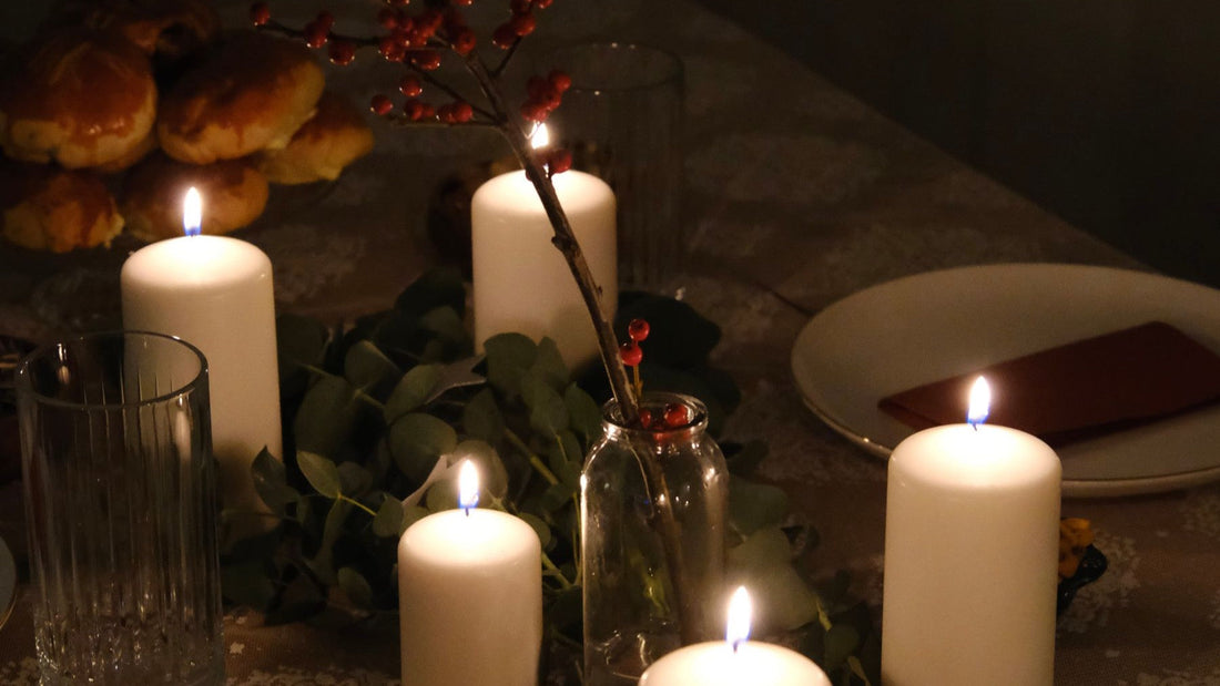 A candlelit winter dinner table is decorated with greenery and red berries for a Christmas in July gathering.