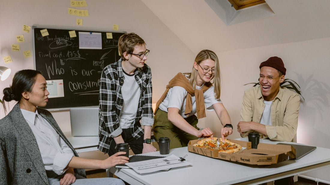 Four colleagues share pizza and coffee during an informal team lunch in their office.