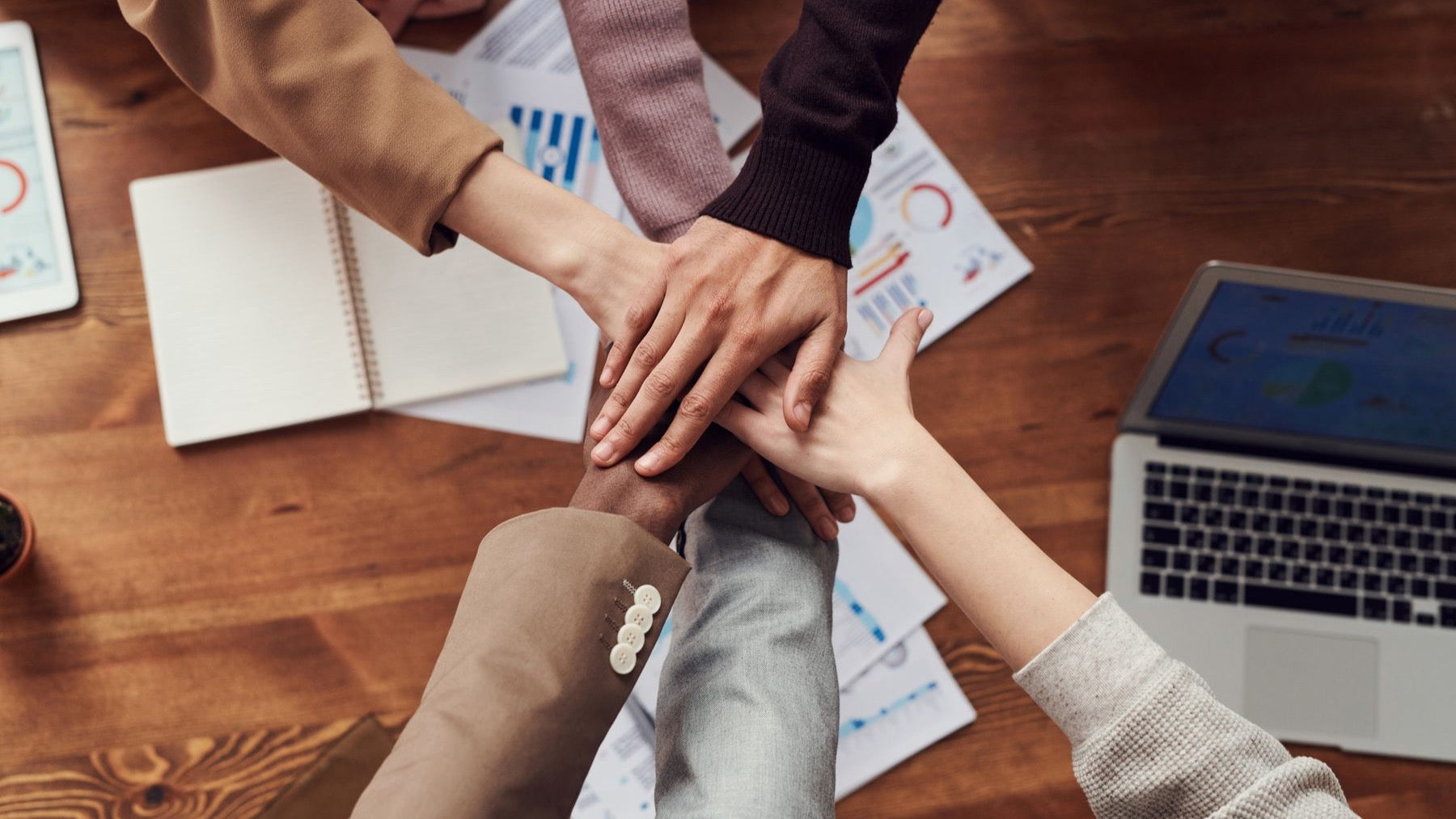 Colleagues stack their hands above a table during a collaborative corporate team session.
