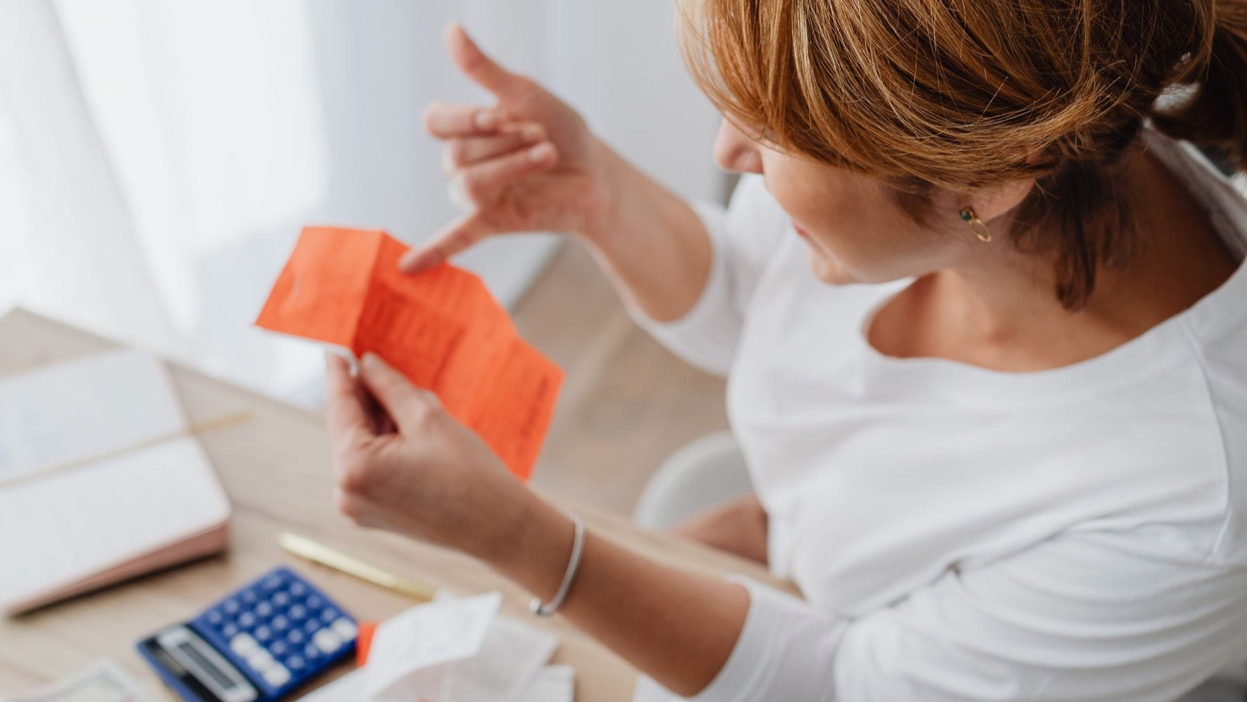 A calculator, receipts and laptop are used to compare household costs at a wooden table.