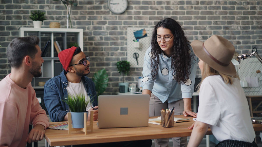 Four coworkers discuss a project around a shared table in a relaxed creative workspace.