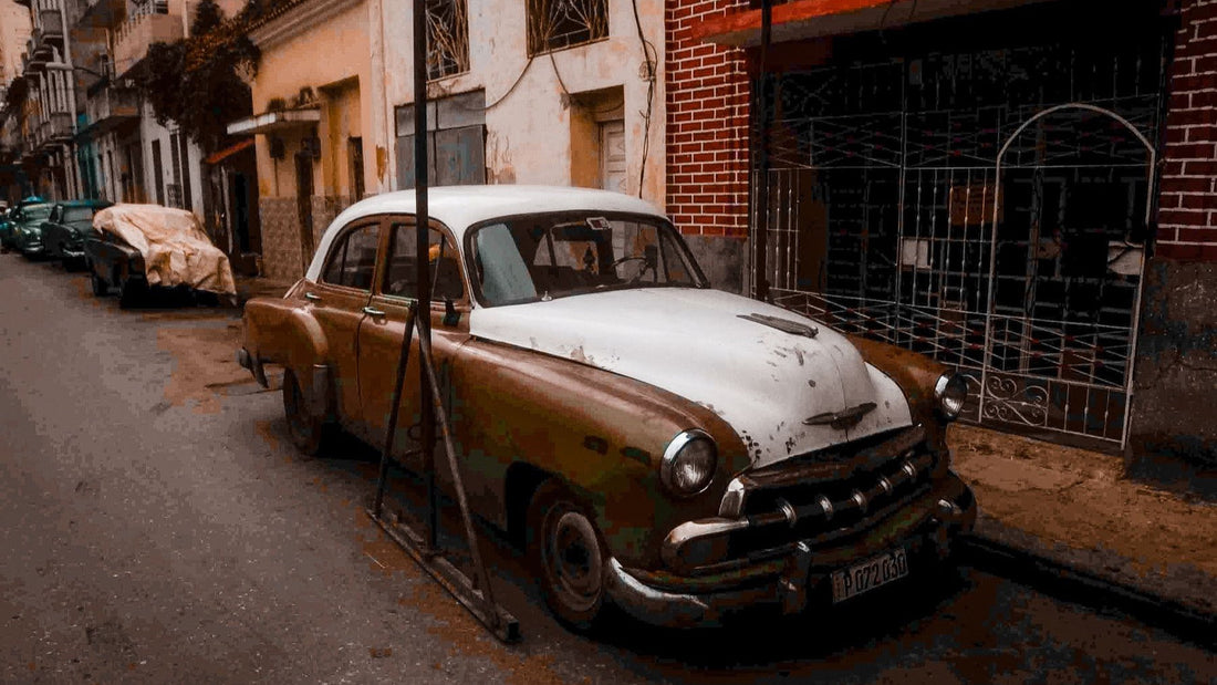 A weathered vintage car is parked on a narrow residential street in Havana, Cuba.