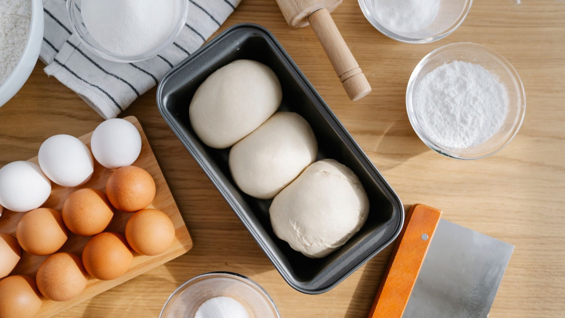 Dough, eggs, flour and a rolling pin are arranged on a kitchen worktop for home baking.