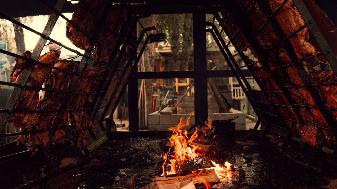 Cuts of meat cook slowly around an open wood fire in a traditional Argentinian asado setup.