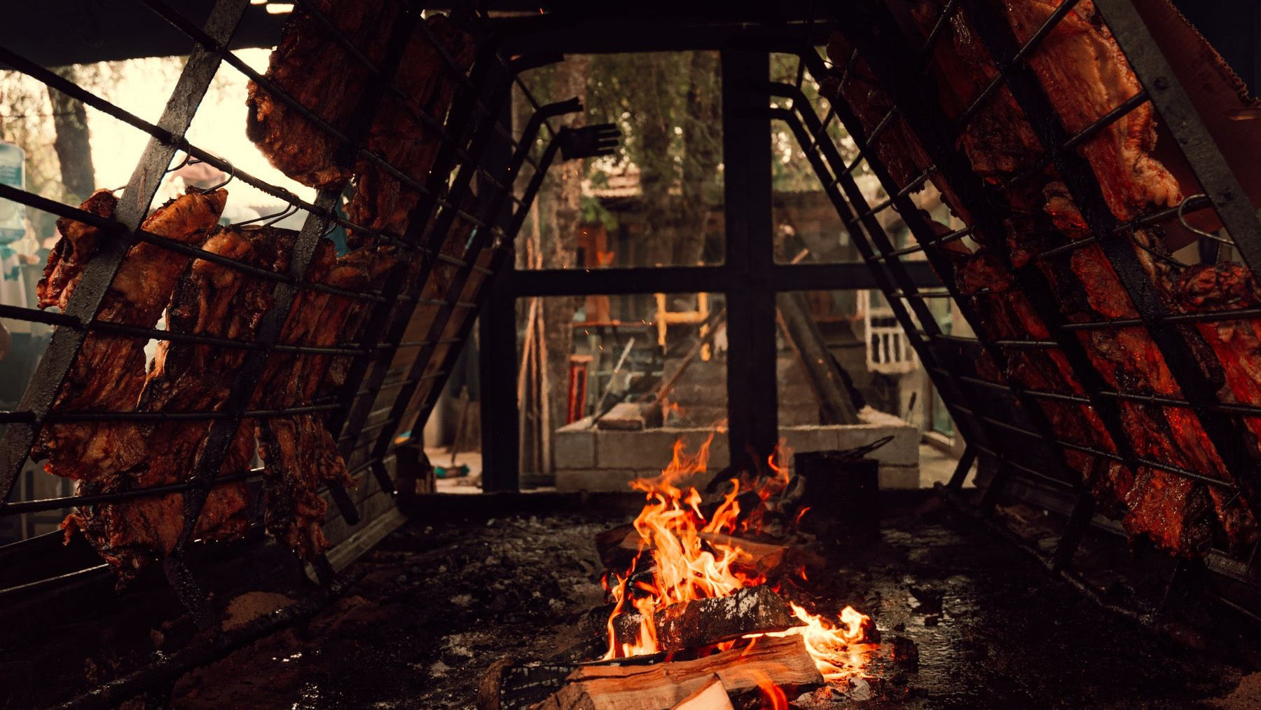Cuts of meat cook slowly around an open wood fire in a traditional Argentinian asado setup.