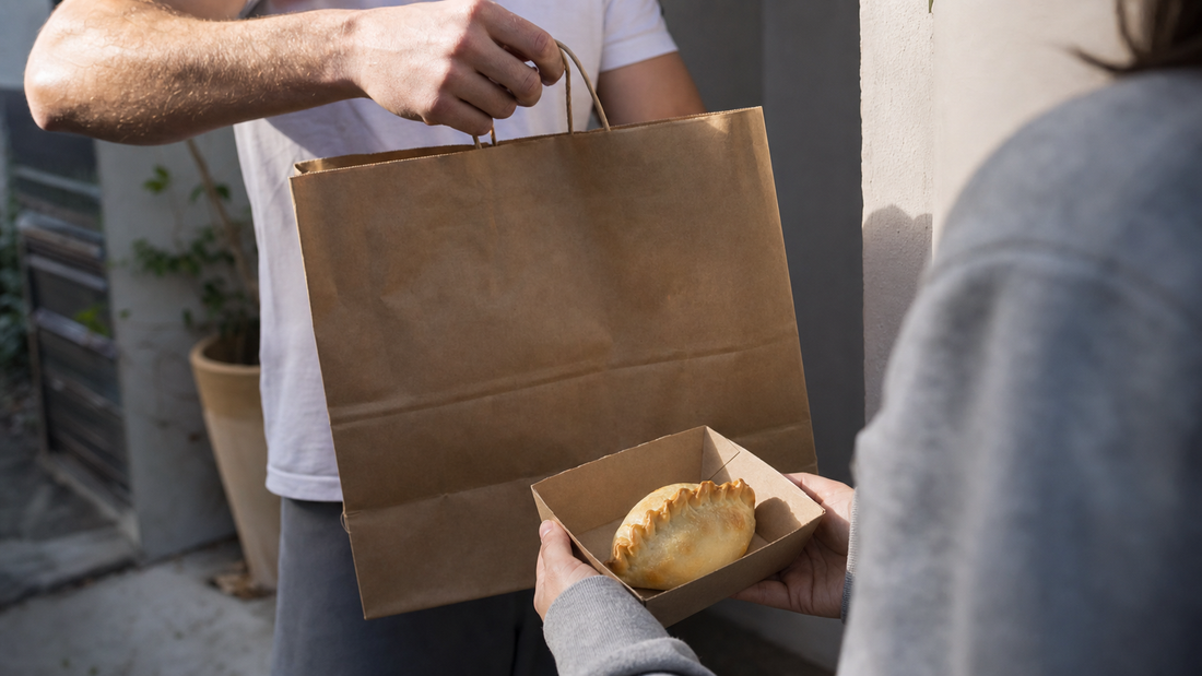 A customer receives an unbranded delivery bag while holding one sealed golden empanada in a paper tray at a Bronte home.