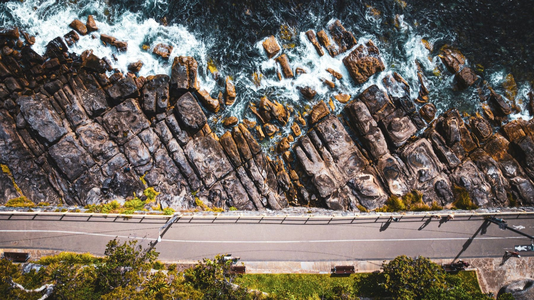 An aerial view shows waves breaking along Manly's rugged coastal road and rocky shoreline.