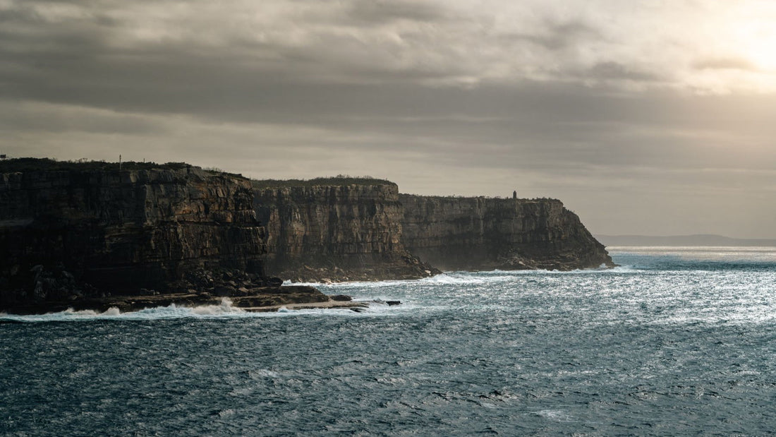 Dramatic sandstone cliffs meet the ocean beneath a moody sky near Sydney Harbour.