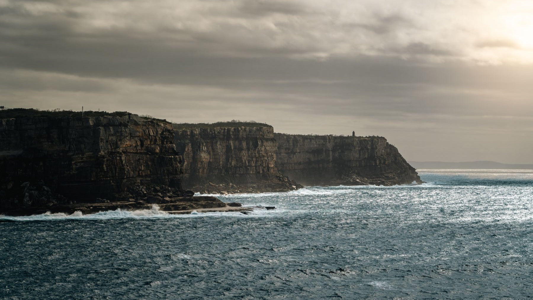 Dramatic sandstone cliffs meet the ocean beneath a moody sky near Sydney Harbour.