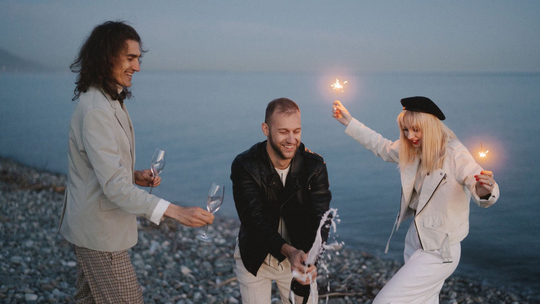 Friends celebrate beside the ocean at twilight with champagne and sparklers.