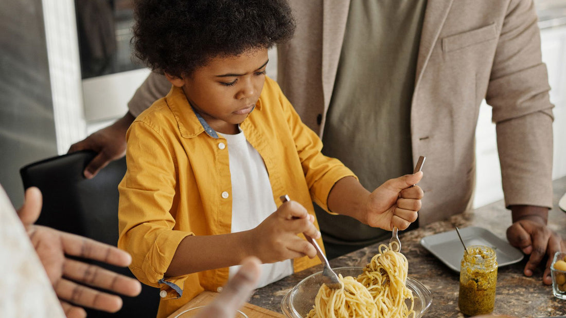 A father and son prepare and share a pasta meal together in their home kitchen.
