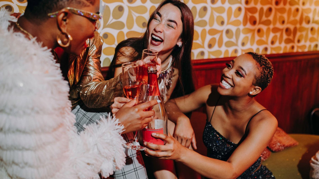 Three friends laugh and raise sparkling drinks during a lively hens party celebration.