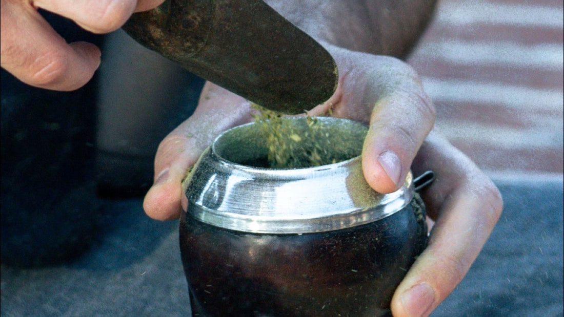 A person scoops loose yerba into a traditional mate gourd during preparation.