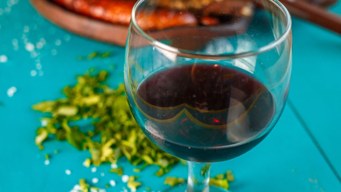 A glass of red wine is served beside an Argentine-style grilled meal on a bright blue table.
