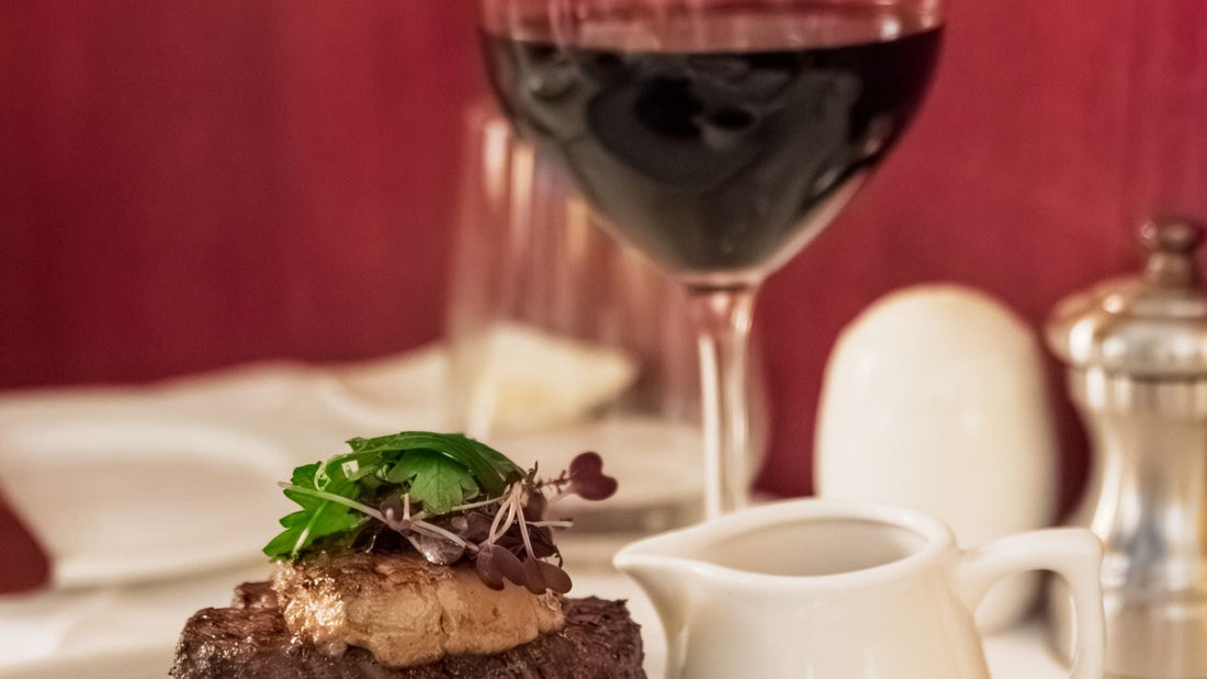 A grilled steak dinner is paired with a generous glass of red wine in a formal dining room.