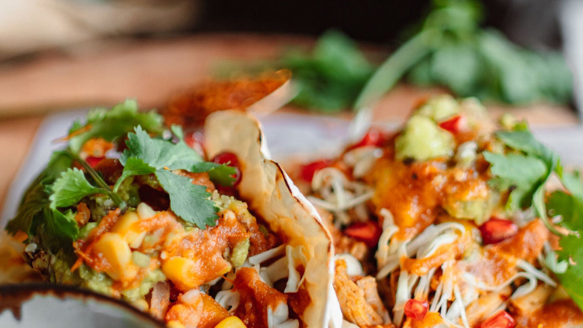 Fresh Mexican tacos are topped with guacamole, corn, salsa and coriander.
