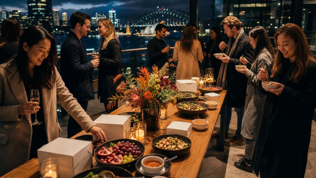 Colleagues gather around salads, fruit, soup and closed catering boxes at a winter rooftop office party overlooking Sydney Harbour.