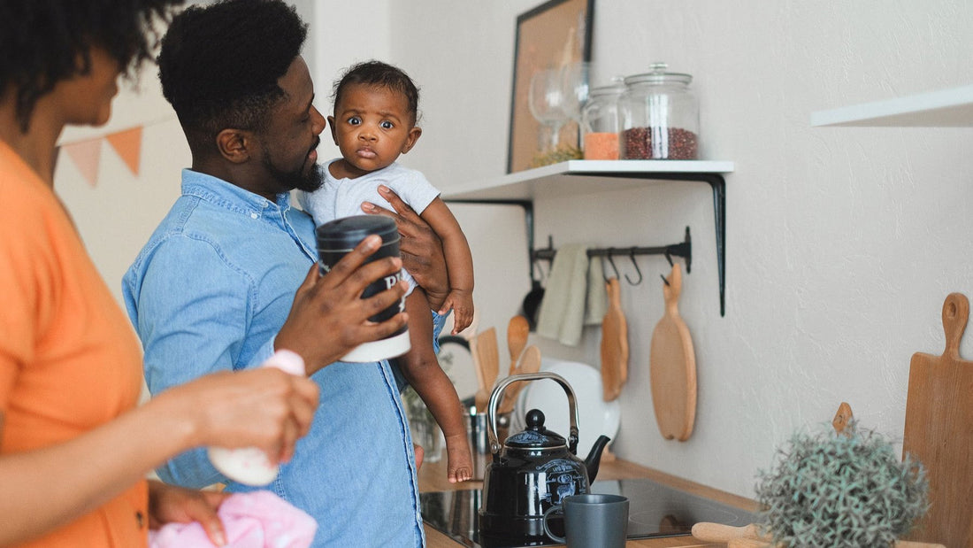 Two new parents share a quiet moment with their baby in a bright home kitchen.
