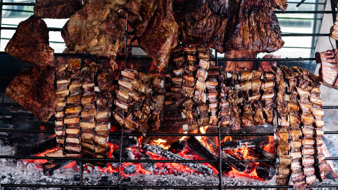 Ribs and assorted beef cuts cook over glowing coals on a traditional Argentinian asado grill.