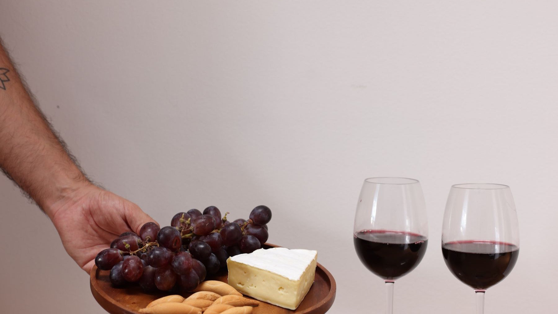Two glasses of red wine are served with grapes, cheese and crackers.