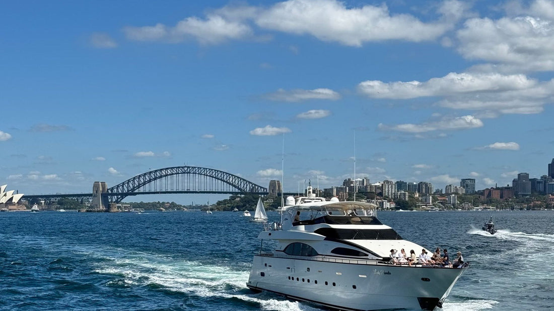 Guests relax aboard a motor yacht crossing Sydney Harbour with the Harbour Bridge behind them.