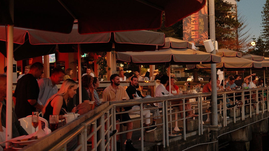 Diners fill a warmly lit waterfront restaurant terrace in Sydney at dusk.