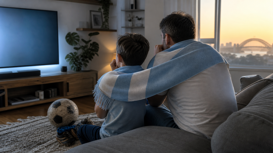 A father and child share a sky-blue-and-white scarf while watching football at dawn in a Sydney living room.