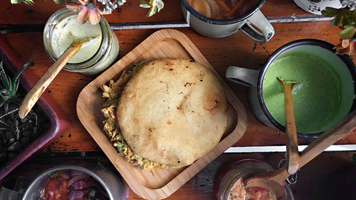 A traditional Venezuelan arepa is served with colourful sauces and condiments on a rustic table.