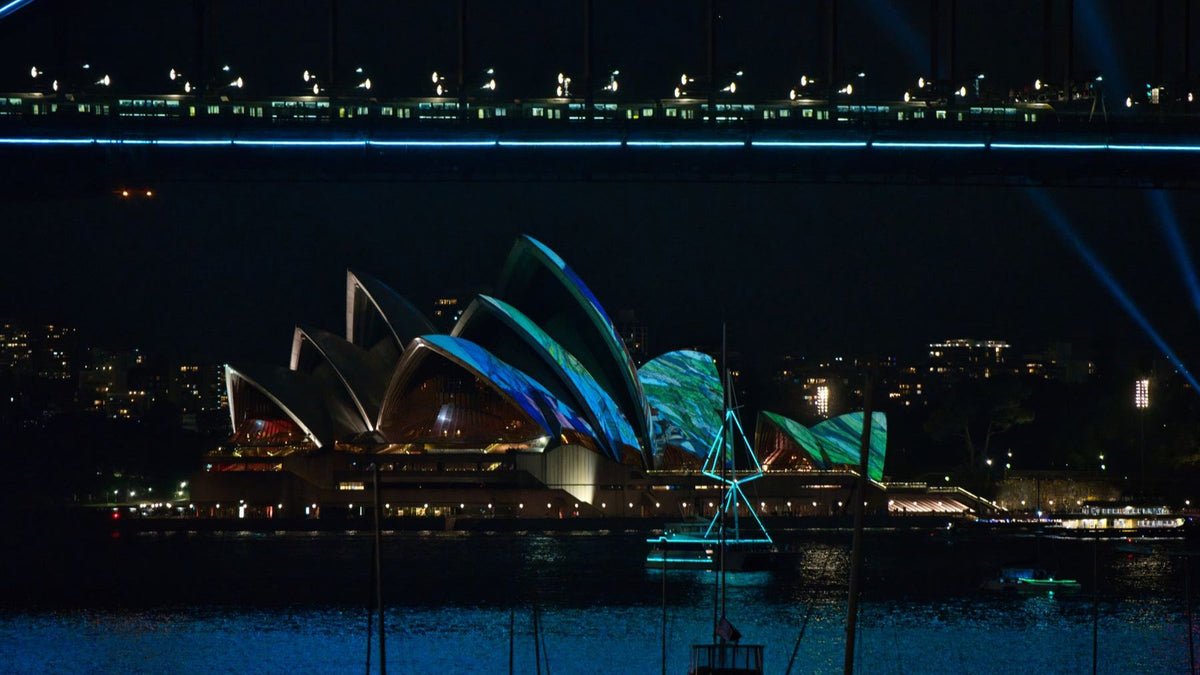 Colourful Vivid Sydney projections illuminate the Sydney Opera House beneath the Harbour Bridge at night.