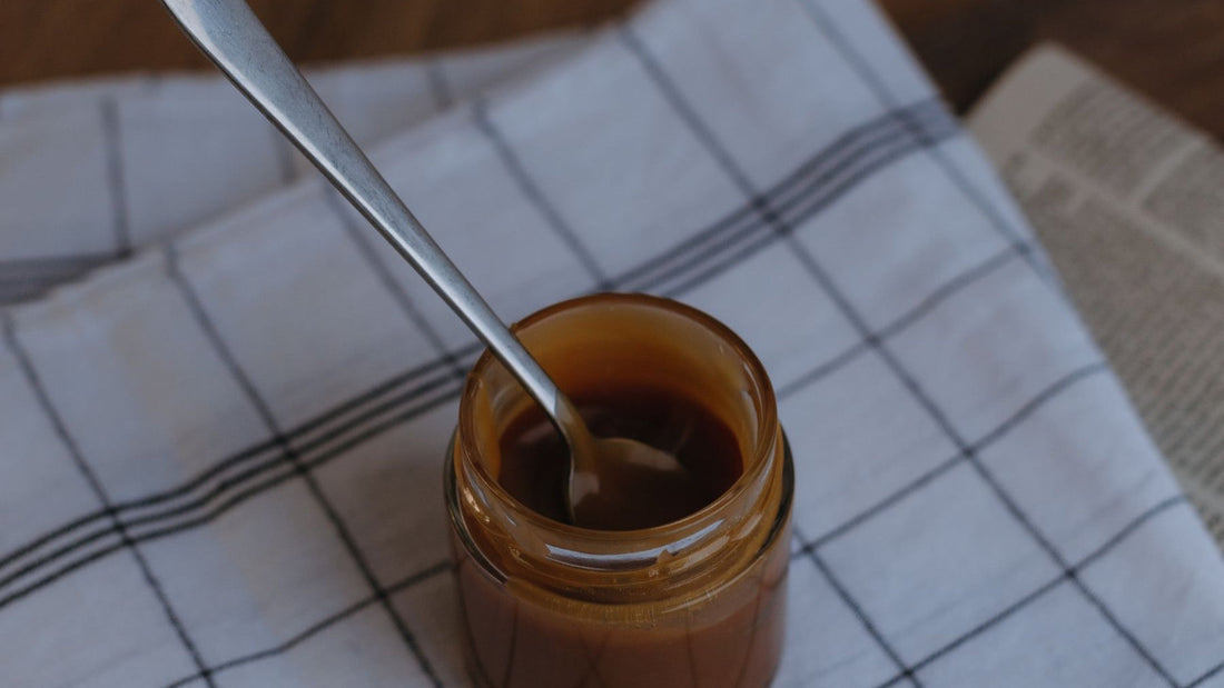 A spoon rests inside a glass jar of thick caramel-coloured dulce de leche.