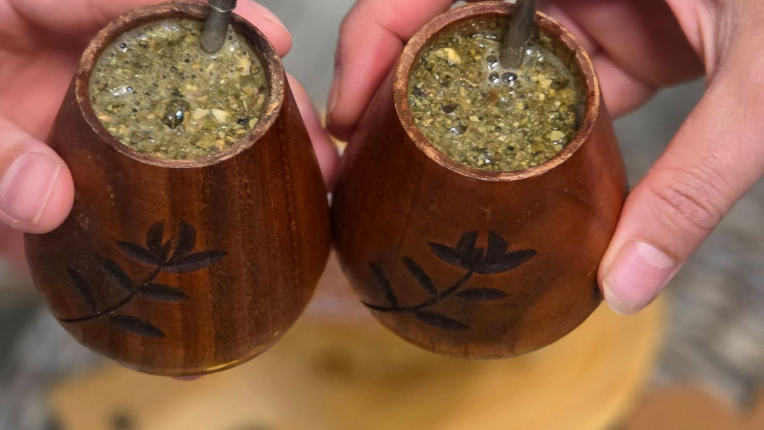 Two people hold traditional wooden mate gourds filled with yerba and fitted with metal bombillas.