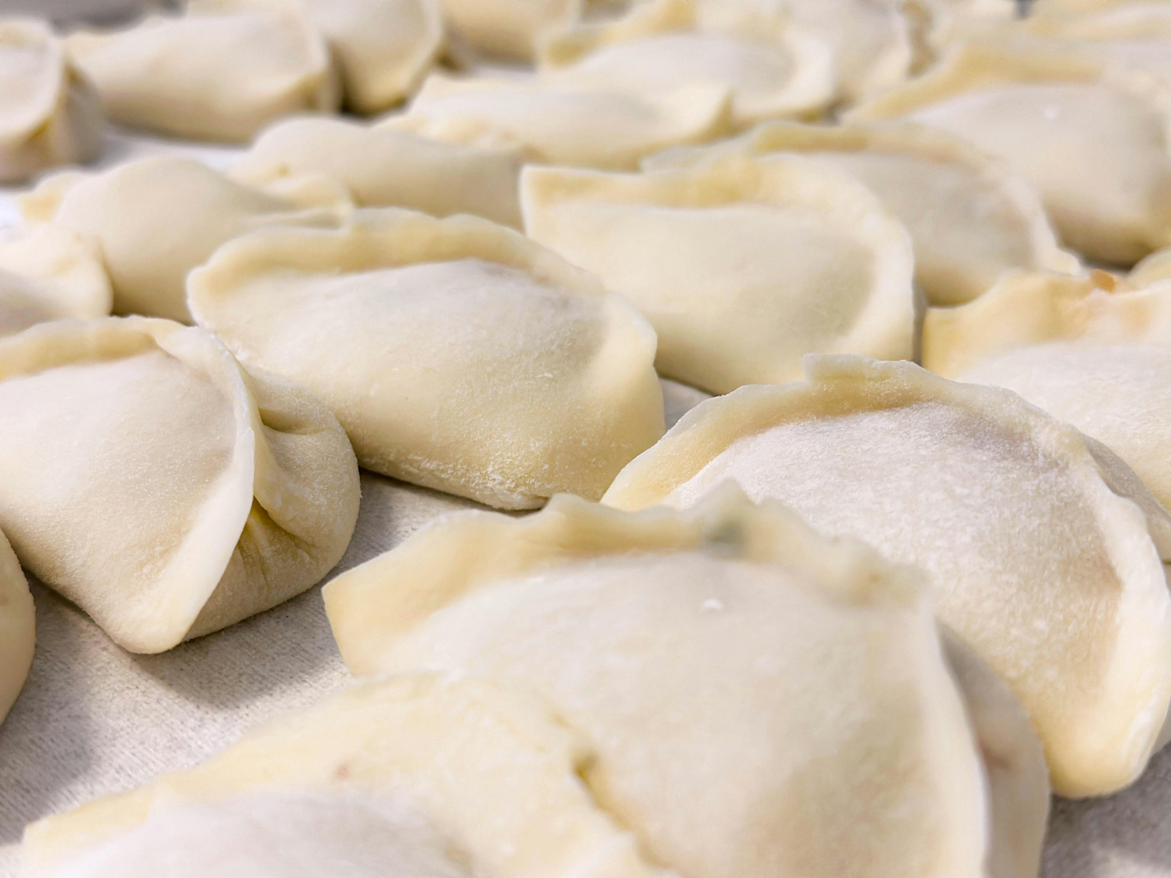 Rows of freshly folded uncooked filled pastries laid out on a flat surface, showcasing the universal hand-formed dough technique shared across world cuisines
