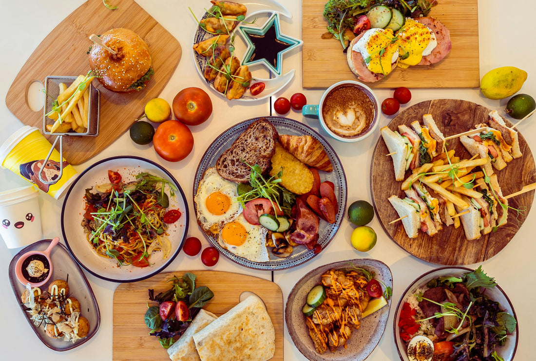 Overhead flat-lay of Australian party food spread including burgers, fried eggs, fries, salads, sandwiches and shared plates on wooden boards