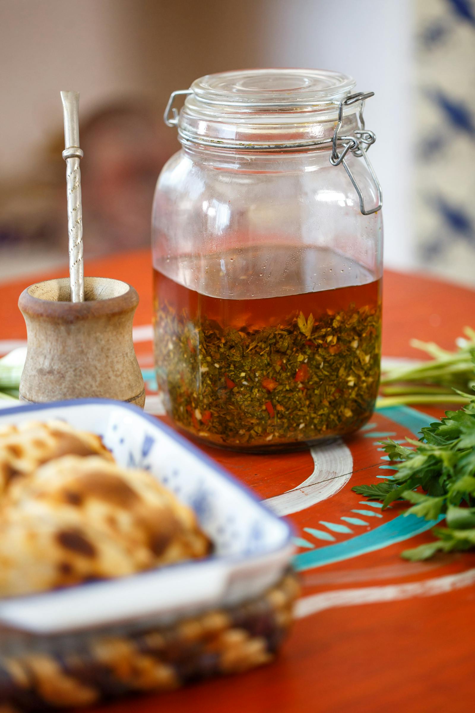 Traditional Argentinian chimichurri sauce in a glass jar beside a mate cup