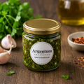 Jar of Argentum Empanadas Chimichurri on a wooden surface with herbs and oil in the background